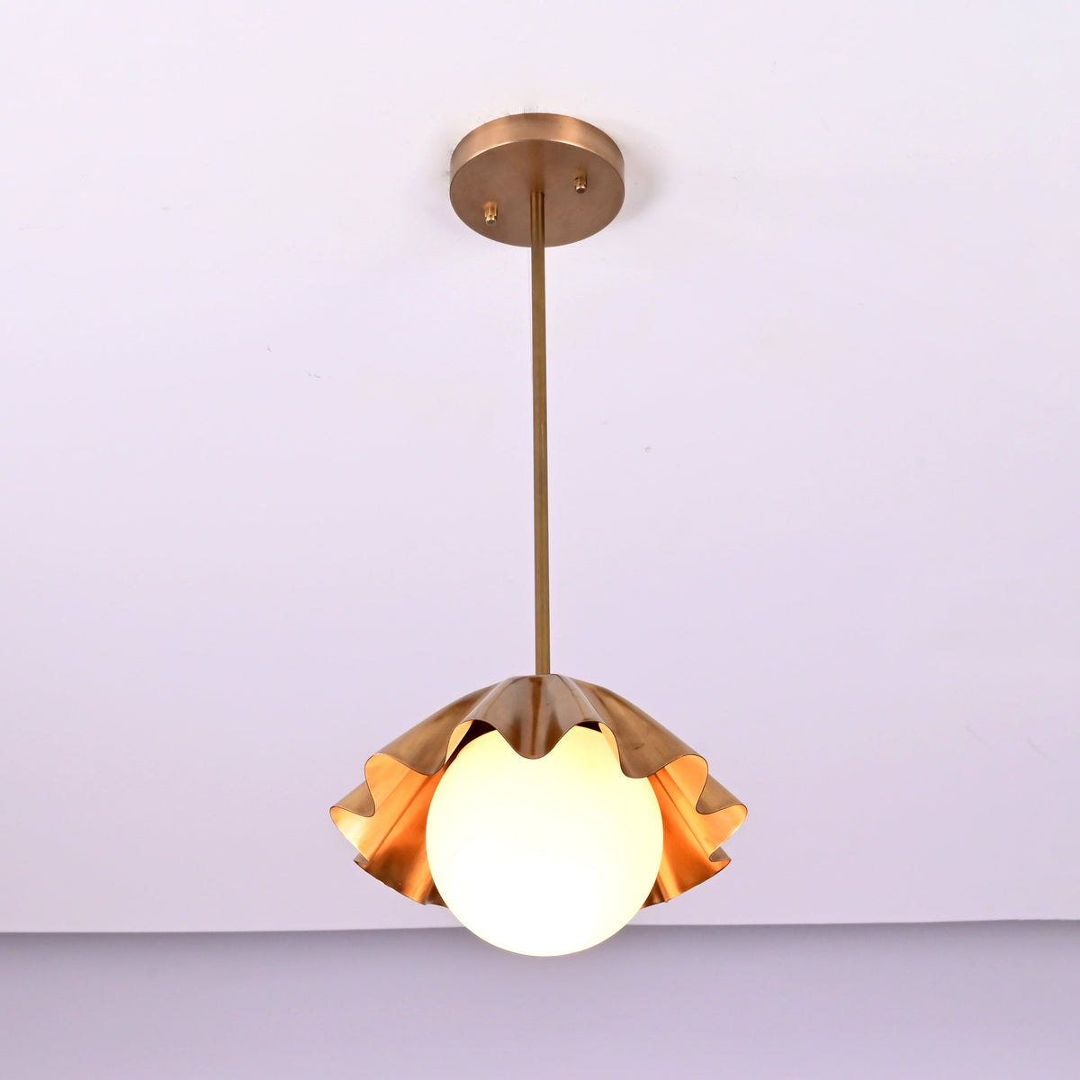 Front view of handcrafted brass disc pendant light with fluted shade and soft warm glow.