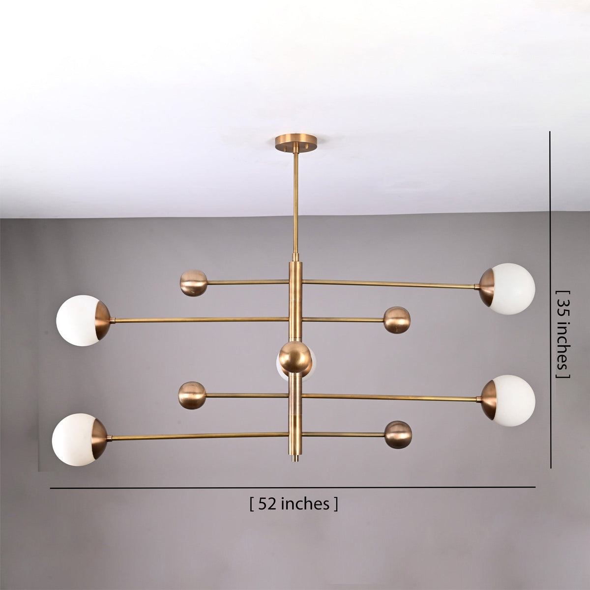 Modern brass globe chandelier shown from below with five opal glass shades and balanced linear arms