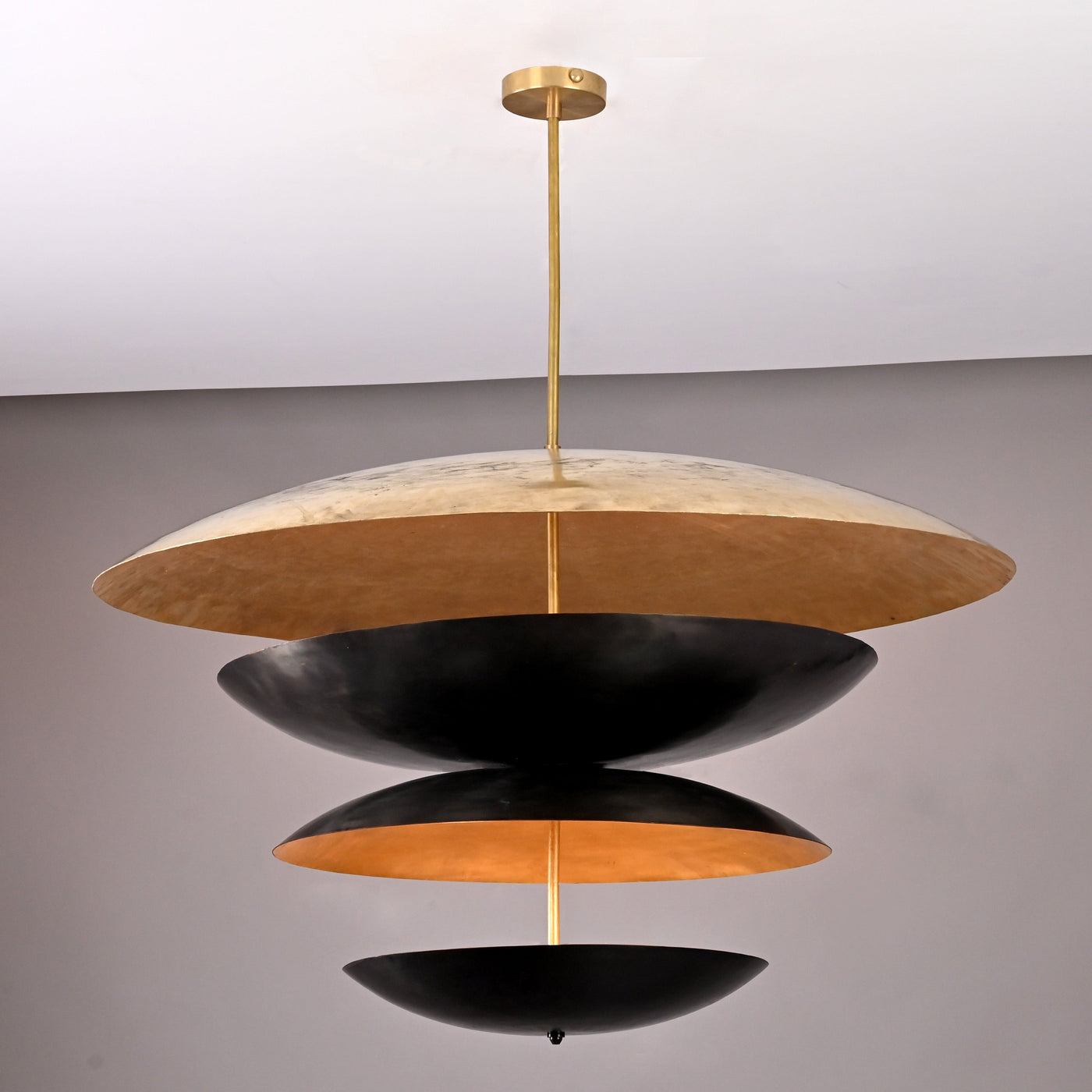 Modern sculptural brass chandelier featuring stacked black and gold discs crafted in a unique layered floating design.