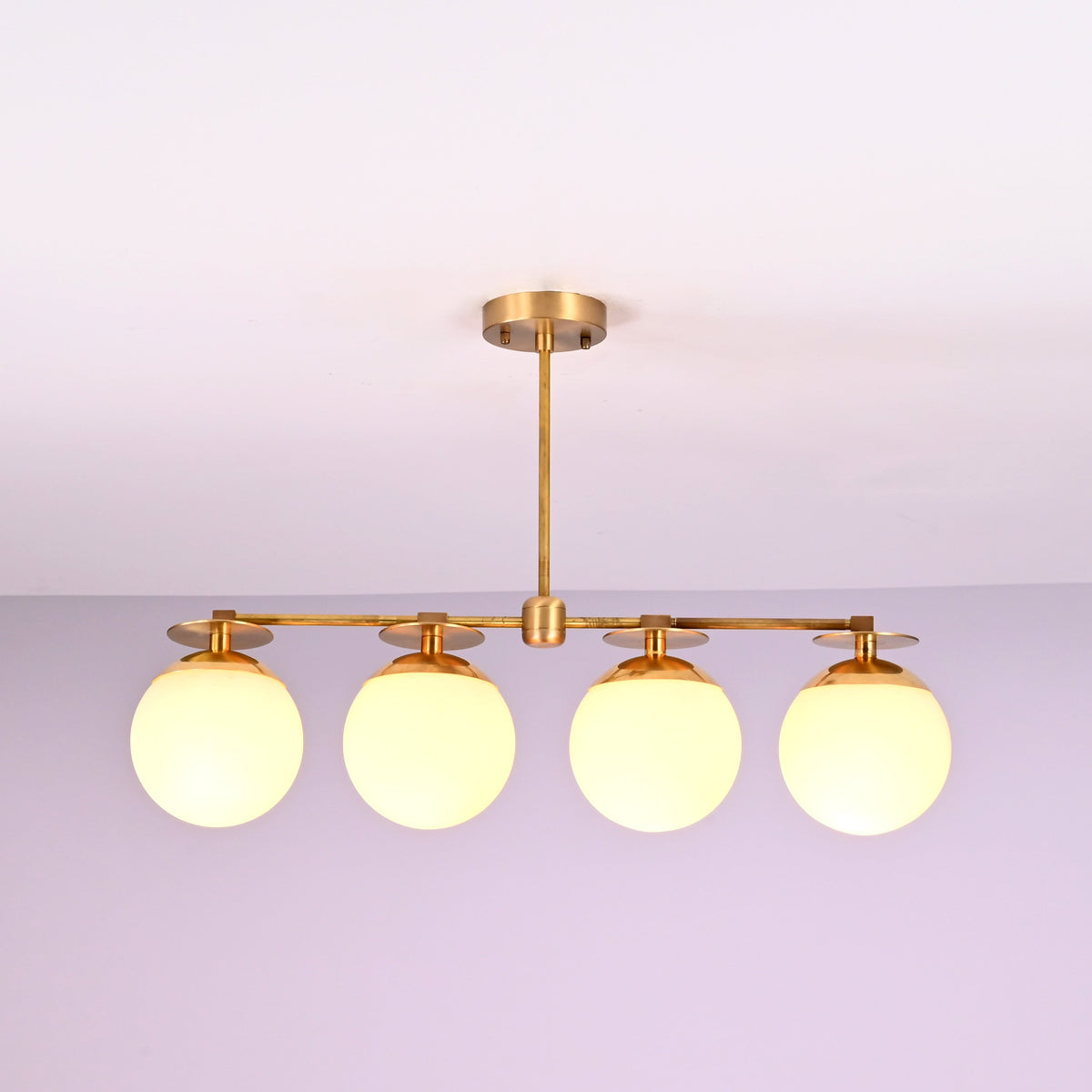 Modern linear brass chandelier with four opal glass globes, designed for dining rooms and contemporary interiors.