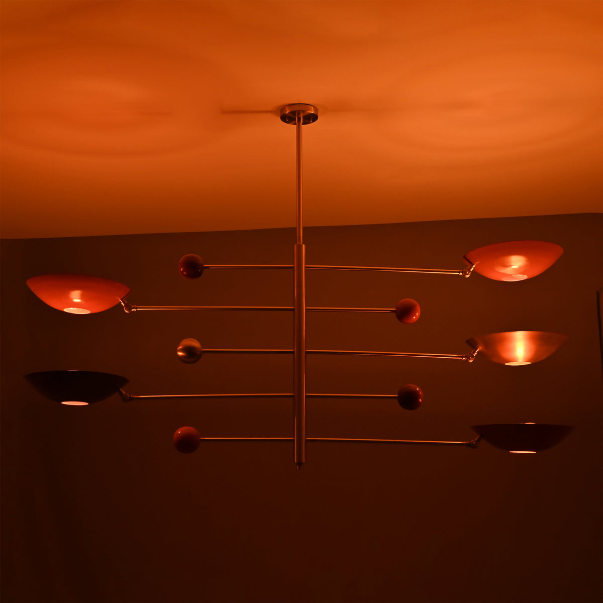 Sculptural modern brass mobile lighting fixture with red bowl shades casting warm ambient illumination.