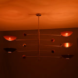 Sculptural modern brass mobile lighting fixture with red bowl shades casting warm ambient illumination.