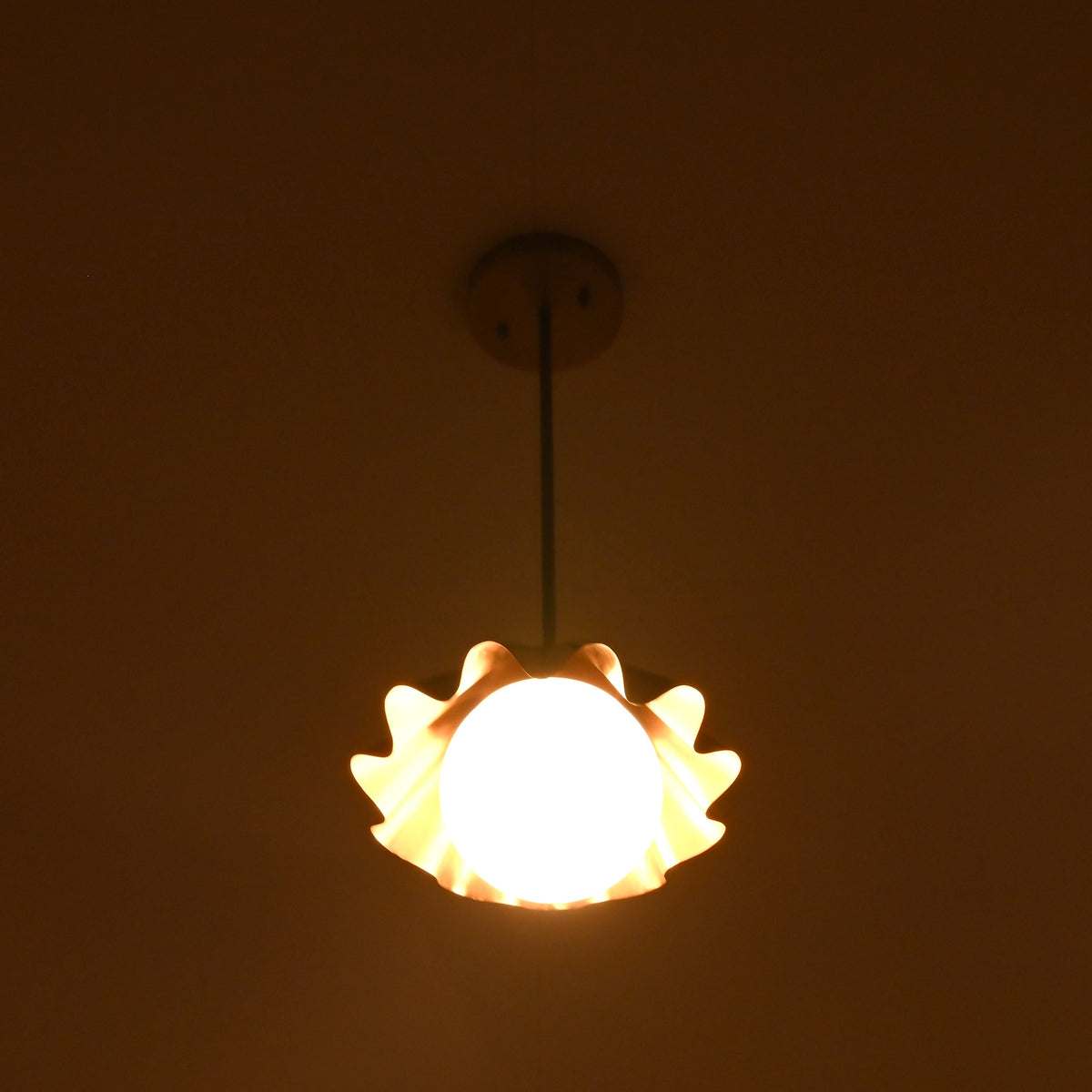 Modern brass pendant light with scalloped shade producing gentle side glow at night.