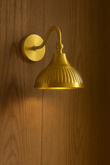 Handcrafted brass dome wall sconce with ribbed detailing installed on white marble wall surface.