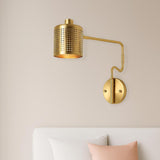 Modern solid brass wall sconce with perforated cylinder shade installed above a bed in a minimalist bedroom