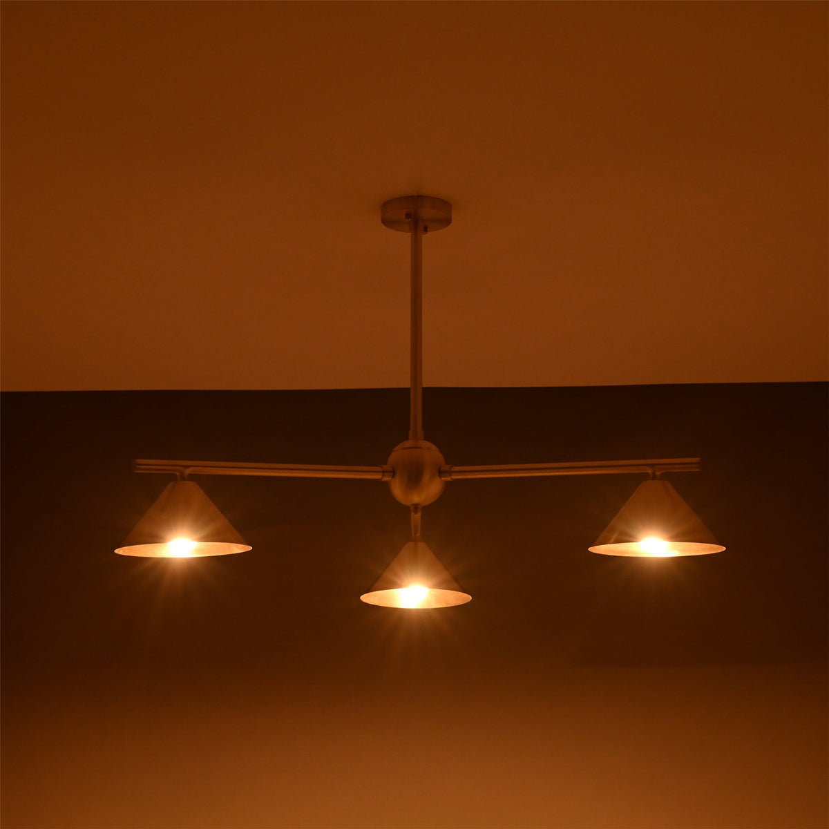Handcrafted brass cone chandelier with three lights glowing softly in ambient warm lighting.