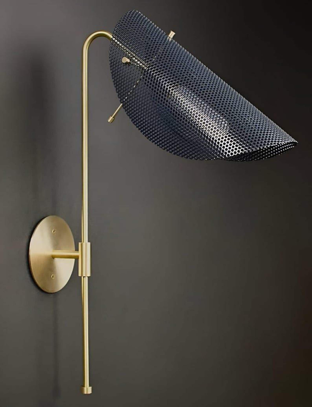 Modern curved brass wall light featuring a perforated metal shade and minimalist silhouette