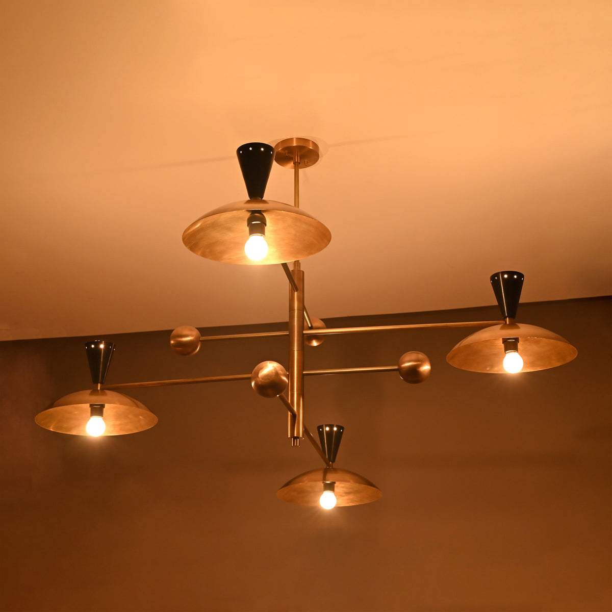 Modern mid-century Diabolo brass chandelier glowing warmly, showcasing black cone tops and bowl-shaped brass diffusers.