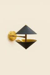 Close side angle of modern industrial brass wall lamp featuring geometric double cone shades and solid brass mounting base.