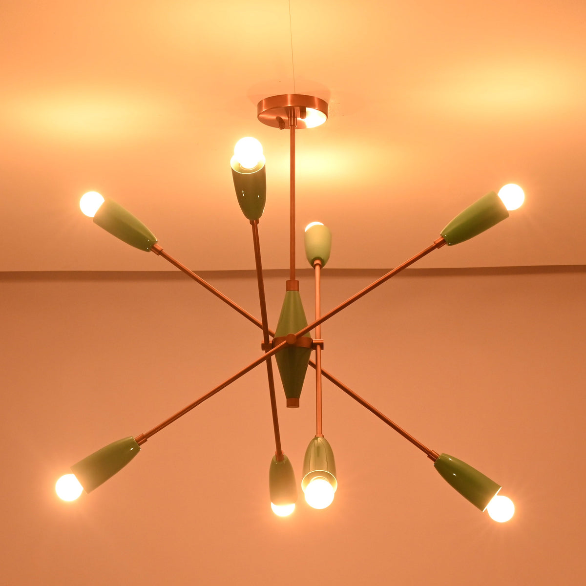Modern mint green brass chandelier illuminated in dark room showing soft halo lighting effect.