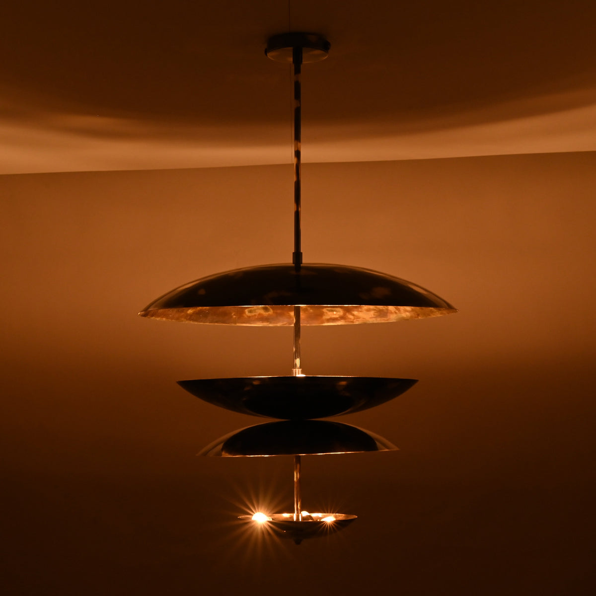 Modern multi-tier brass disc chandelier producing warm indirect light and sculptural glow