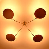 Modern red disc brass ceiling light photographed in low light environment highlighting warm glow and sculptural design.