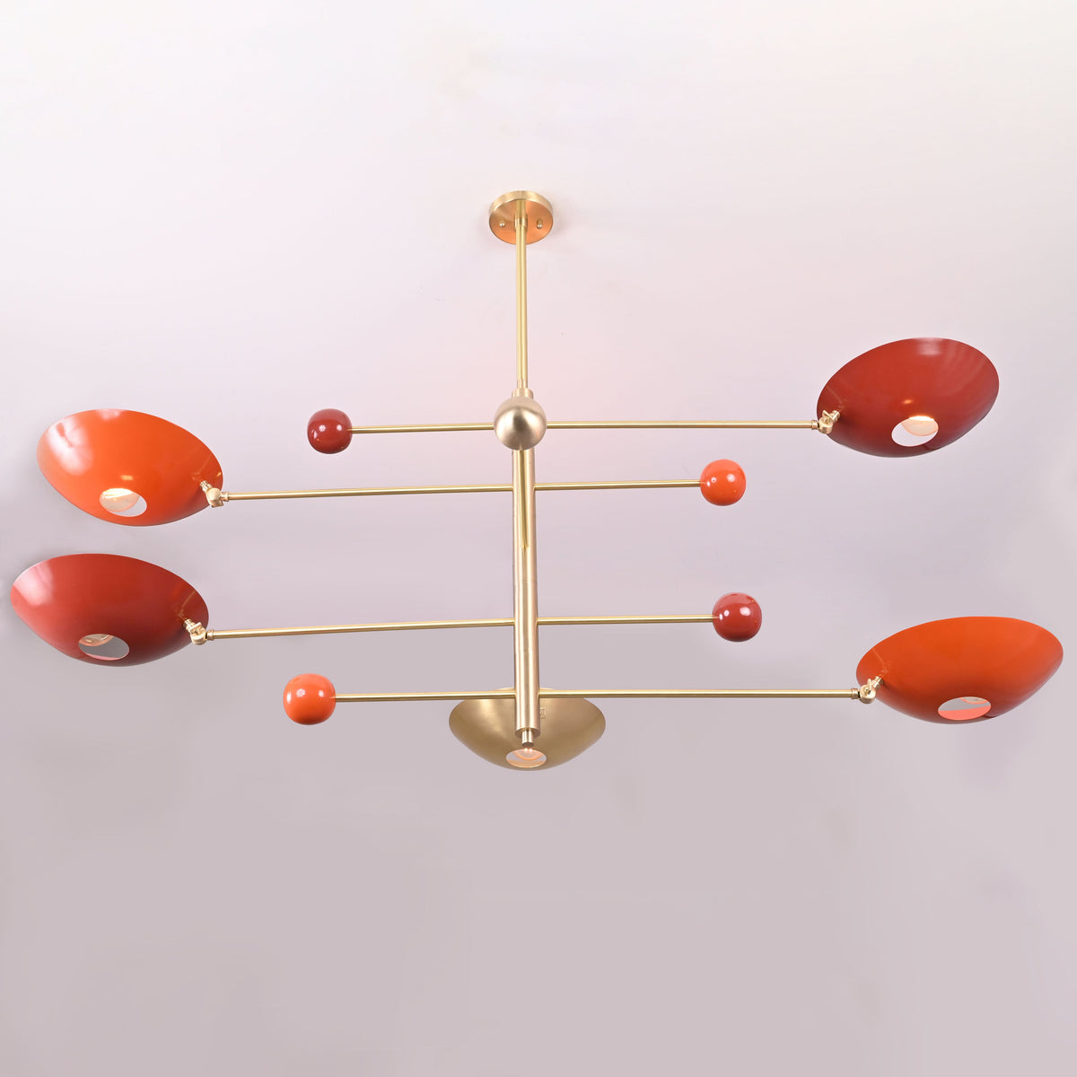 Modern sculptural chandelier in brushed brass with red bowl shades providing upward indirect lighting.