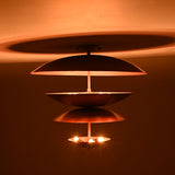 Closeup lit view of the multi-tier brass flushmount chandelier, featuring layered bowls and warm glowing indirect illumination from the lower lights.
