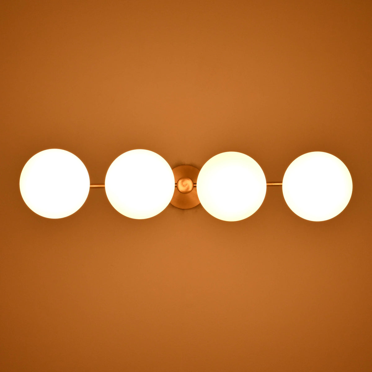 Opal glass globe shades on a brass linear chandelier glowing softly in a dark interior environment.