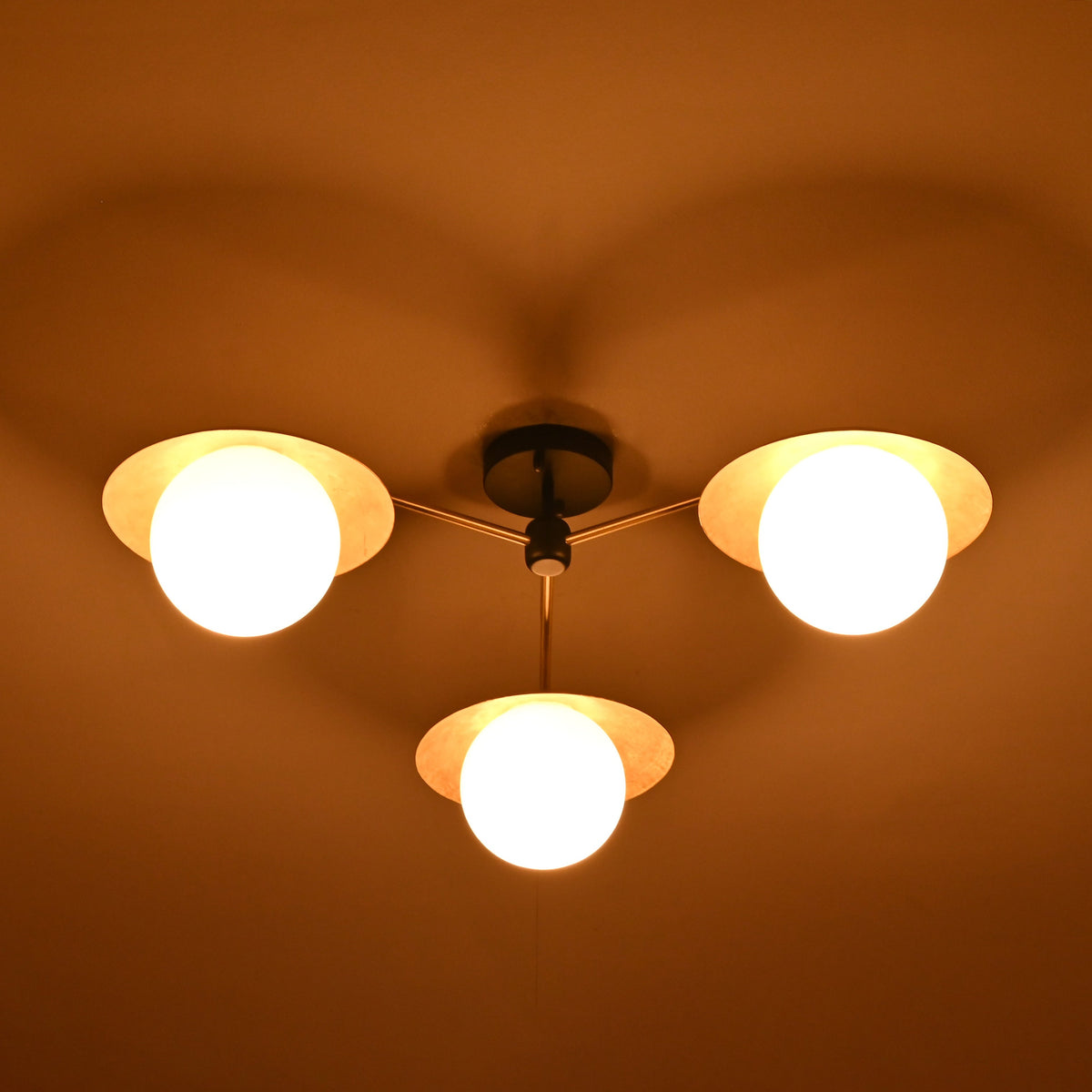 Night view of 3 light brass disc ceiling fixture with opal glass globes creating ambient lighting.