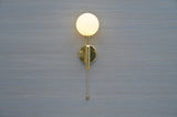 Front view of polished brass wall sconce with opal glass globe and pull chain by Brass Leaf Studio