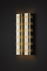 Polished brass perforated wall sconce with warm indirect light displayed against dark background