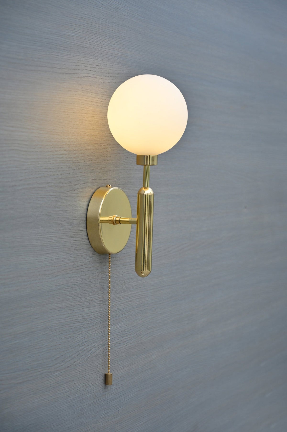 Side view of modern polished brass wall sconce featuring opal glass globe and elegant pull chain switch
