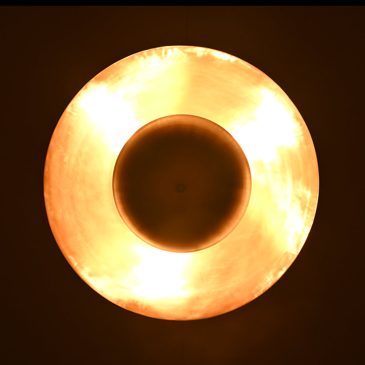 Illuminated top view of brass disc pendant showing soft golden ambient light and radiant metal reflection
