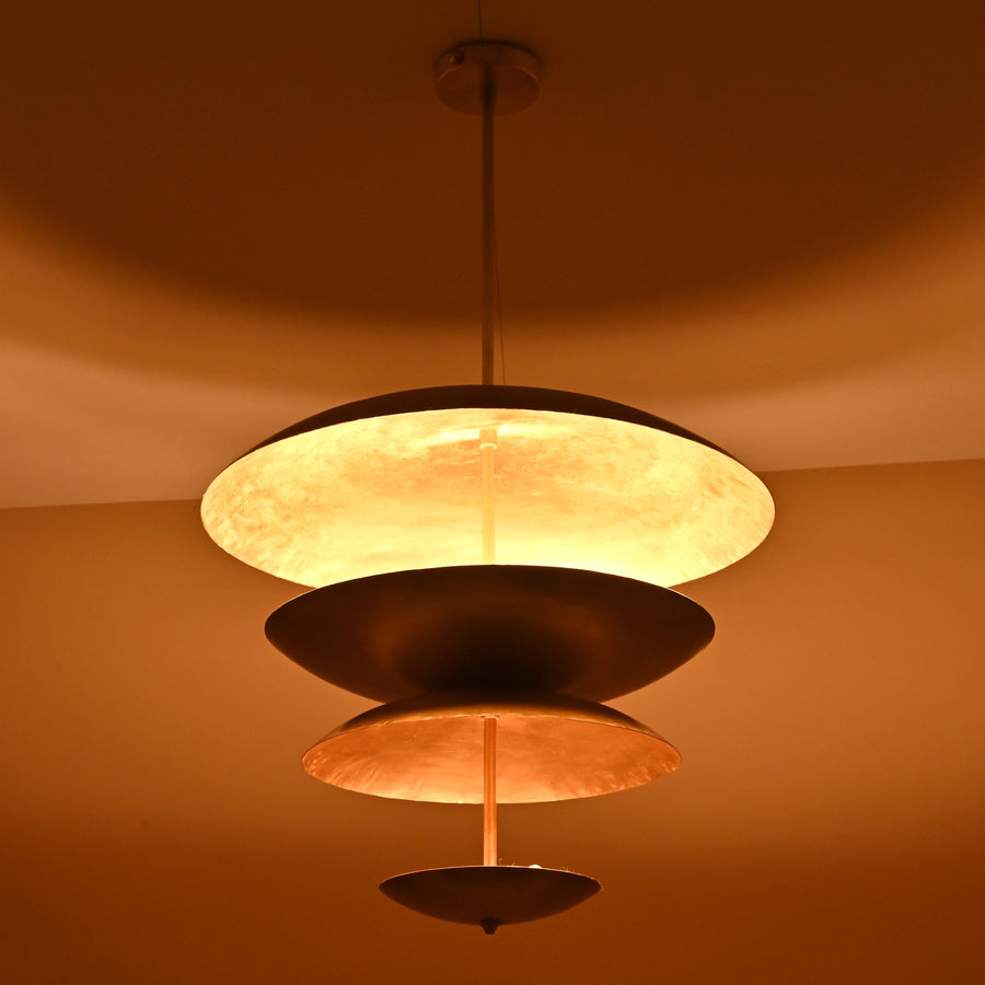 Handcrafted solid brass ceiling light with stacked bowl discs emitting a warm, ambient glow
