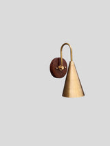 Minimalist brass wall sconce featuring a brushed cone shade and wooden backplate designed for modern interiors by Brass Leaf Studio.