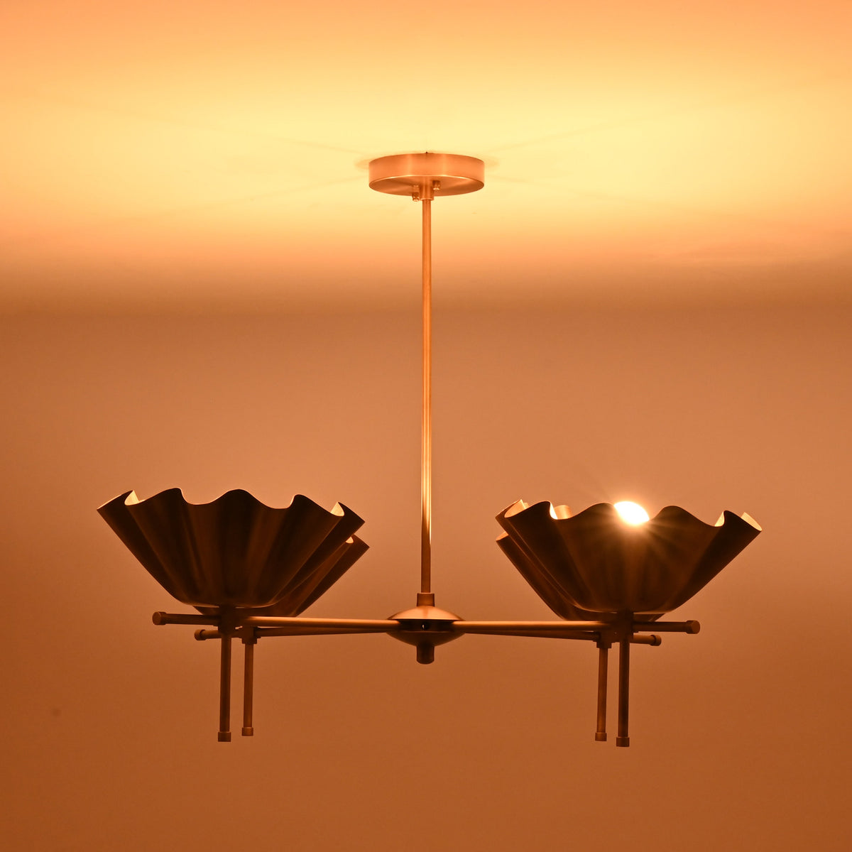 Close view of brass scalloped bowl chandelier casting warm indirect lighting in dark interior