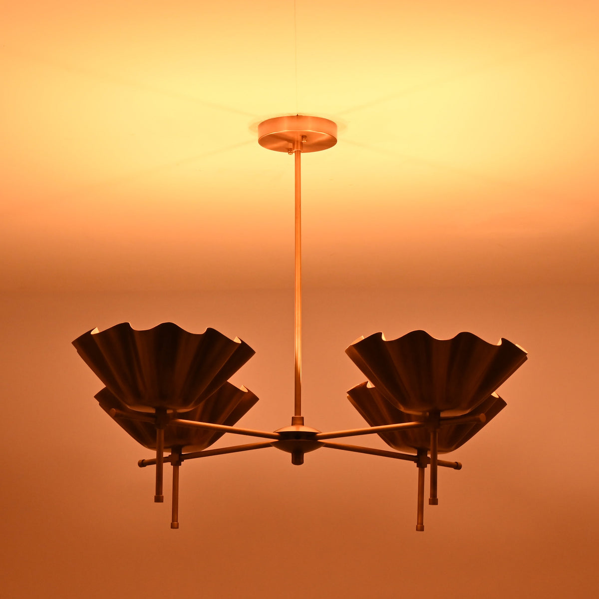 Side view of brass shell shade chandelier illuminated in low light for atmospheric effect