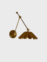 Angled view of adjustable brass swing arm wall sconce with scalloped shade and round wall plate.