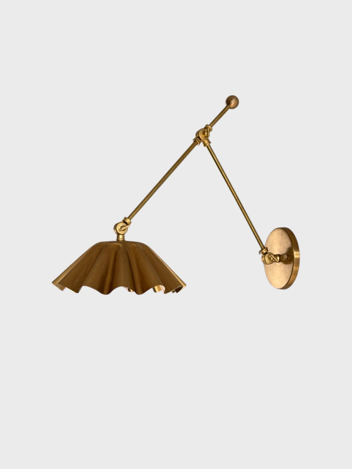 Side profile of brass swing arm wall sconce showing long adjustable arm and scalloped metal shade.