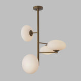 Side angle of a sculptural brass chandelier with milky glass globe shades, highlighting vertical form and softly diffused lighting.