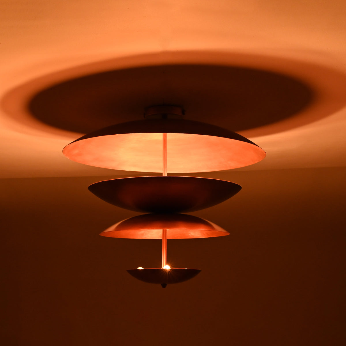 Warm ambient view of the sculptural tiered brass chandelier casting soft indirect light and creating circular shadow halos on the ceiling.