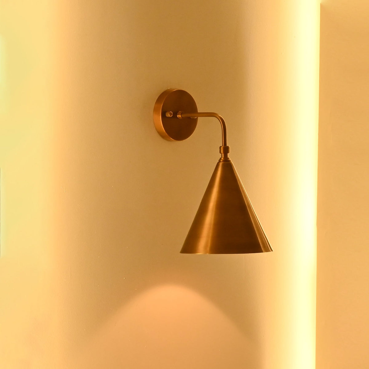Brass cone wall light displayed in a clean arched wall niche with warm architectural lighting