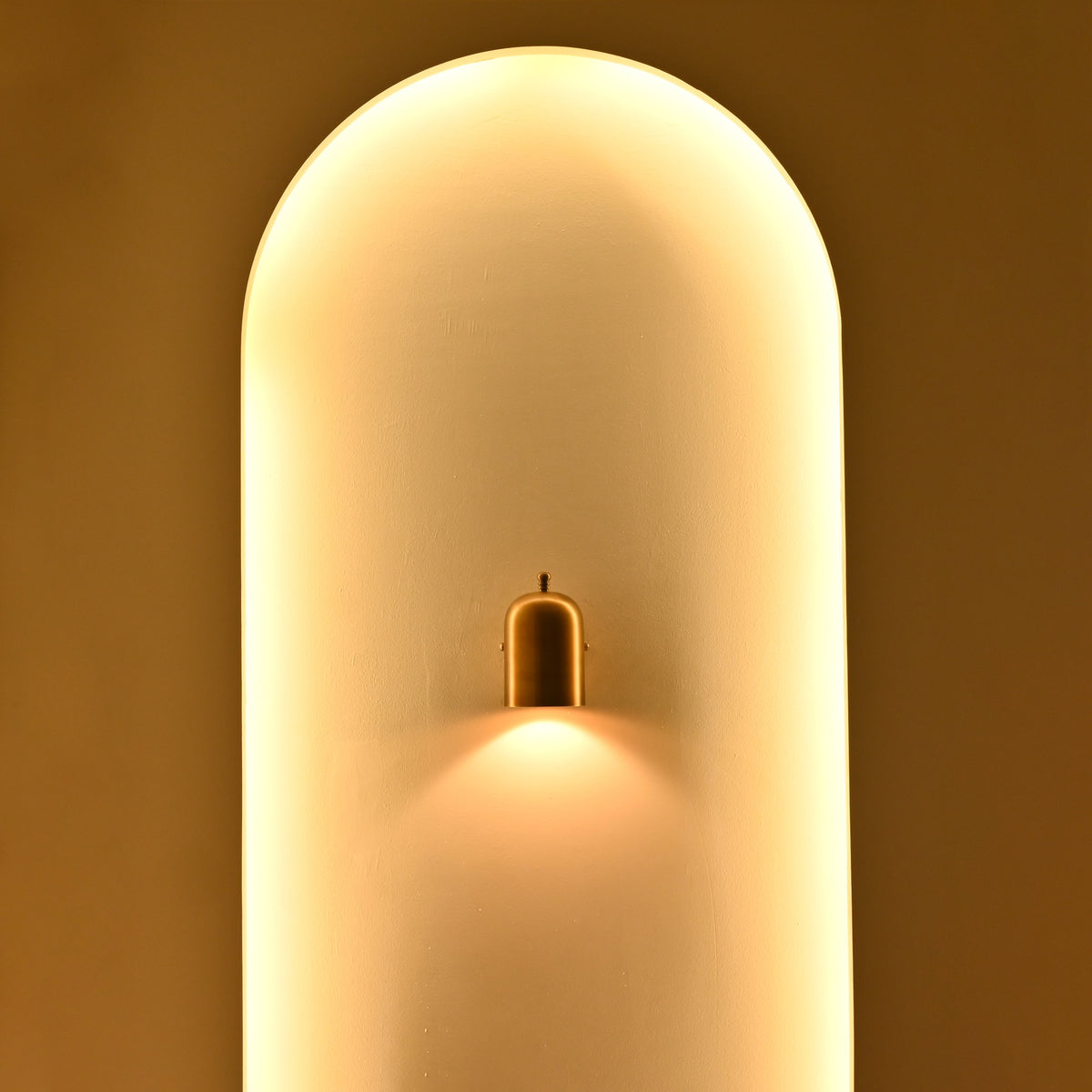 Solid brass cylindrical bedside wall sconce with decorative top finial and warm downward accent lighting