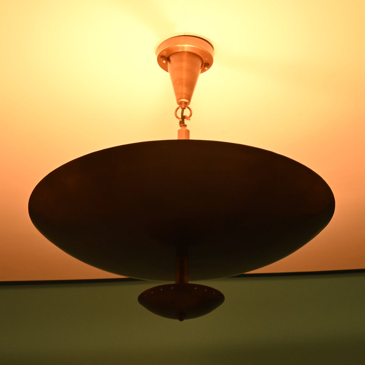 Solid brass bowl chandelier emitting warm indirect light with a refined modern silhouette and atmospheric ceiling illumination