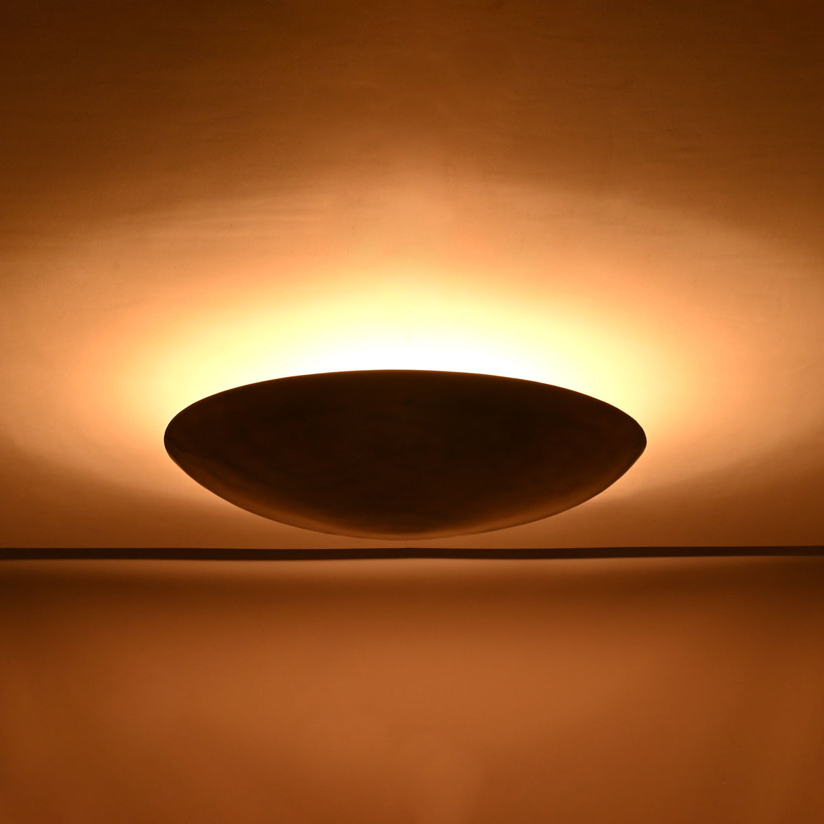 Solid brass bowl flush mount ceiling light shown from front with warm indirect lighting effect