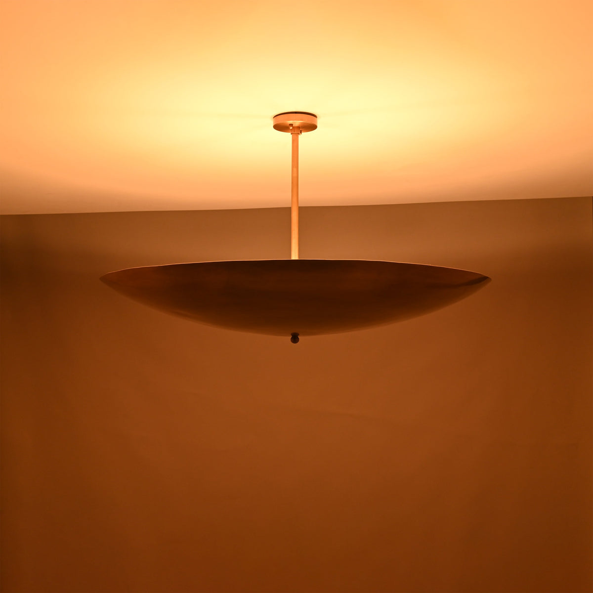 Solid brass disc pendant light illuminated at night with a warm golden glow and indirect lighting.