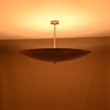 Solid brass disc pendant light illuminated at night with a warm golden glow and indirect lighting.