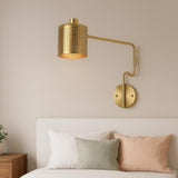Close-up of solid brass wall sconce with perforated metal shade and swing arm design