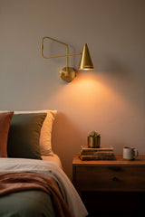 Solid brass swing arm sconce shown illuminated with warm downward glow and tapered cone shade