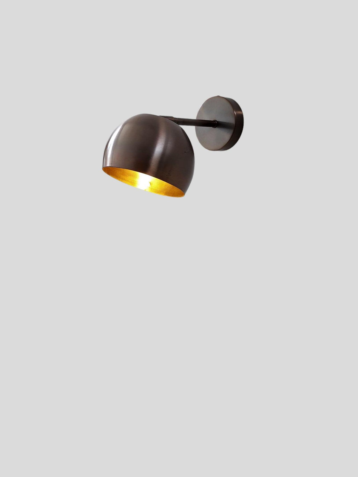 Solid brass wall sconce in antique patina finish with light on, showing warm ambient illumination