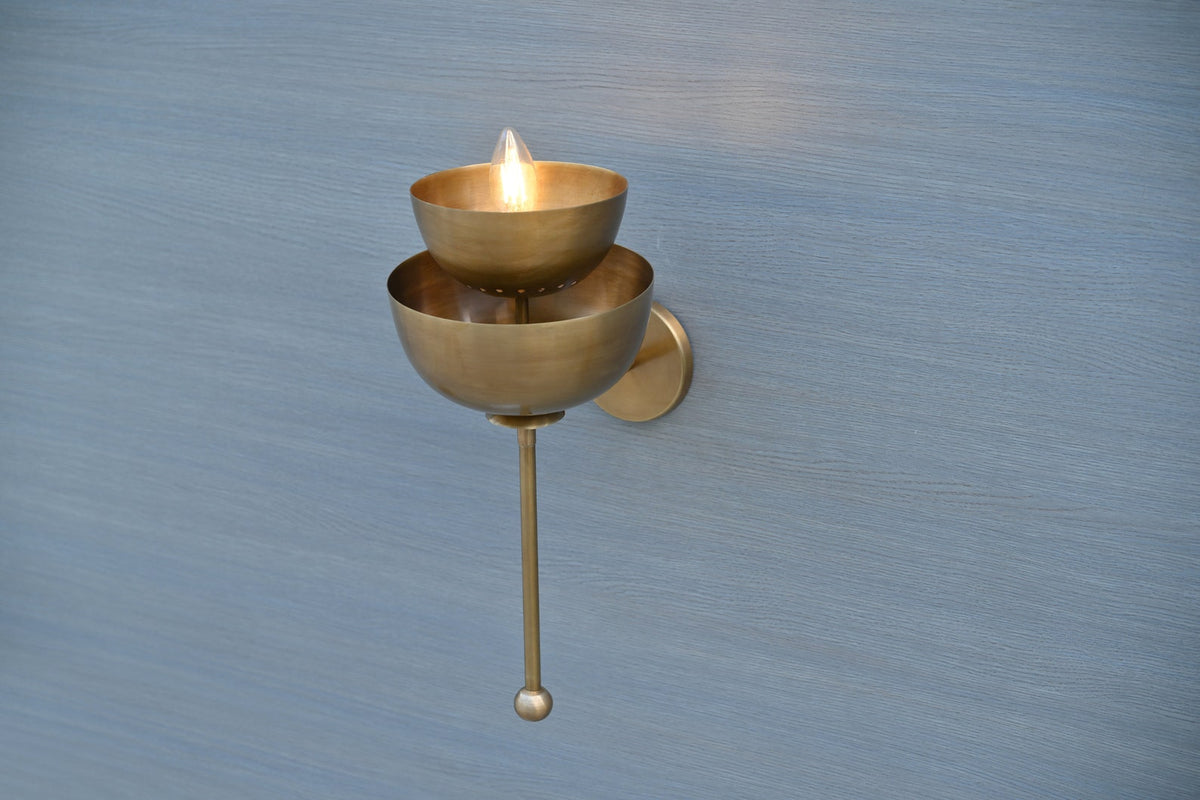 Angled view of handcrafted brass wall sconce with unique stacked bowl design, warm glowing ambient wall light