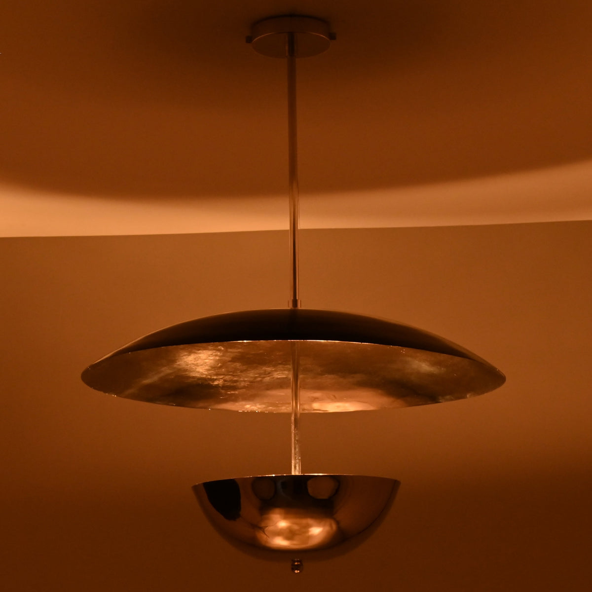 Suspended chrome disc and bowl chandelier glowing warmly in a dimly lit room