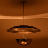 Suspended chrome disc and bowl chandelier glowing warmly in a dimly lit room