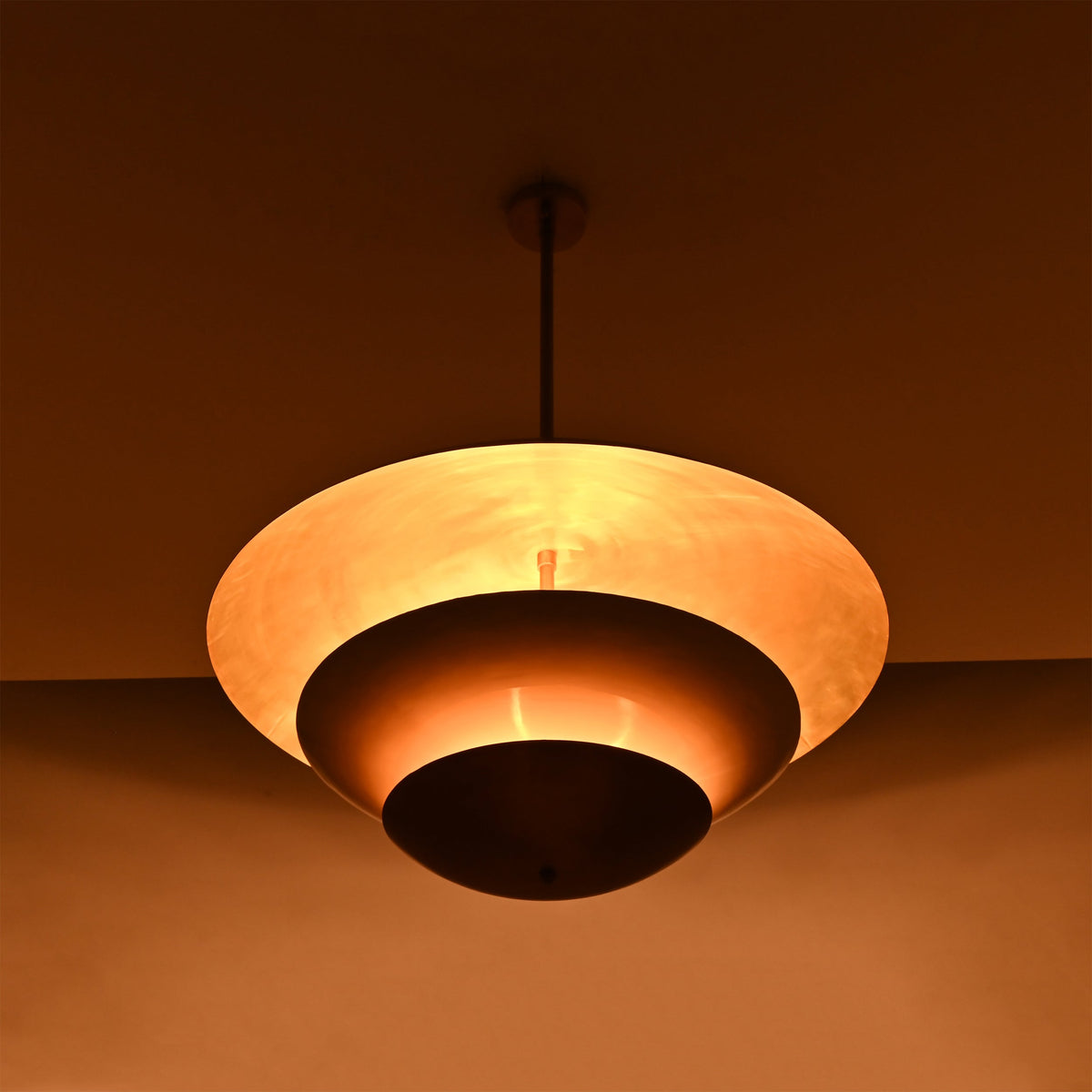 Tiered brass pendant light installed above a bedroom, creating soft warm ceiling light with elegant layered style