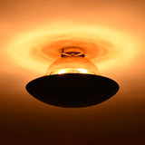 Two-tone brass ceiling light illuminated in low light, revealing polished brass upper dome and blackened disc with warm ambient glow.