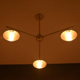Brushed brass 3-light chandelier illuminated in warm ambient lighting, showcasing cone shades in a dark room.